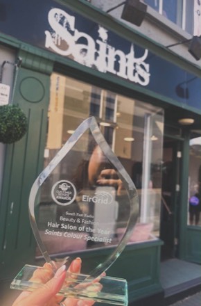 A glass South East Radio award engraved "Hair Salon of the Year, Saints Colour Specialist", held up outside the Saints shopfront.