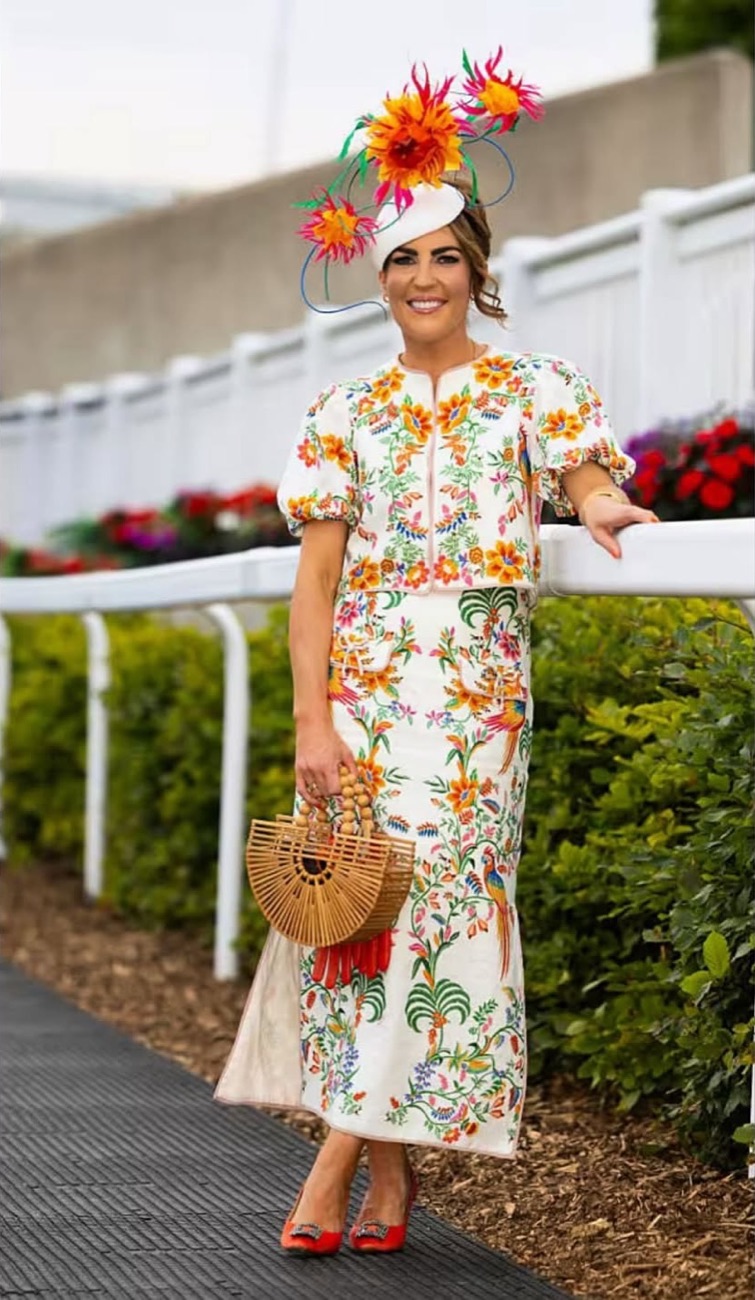 Louisa Murphy at Tramore racecourse in an embroidered floral top and skirt, with a sculptural orange and pink flower headpiece and a bamboo bag.